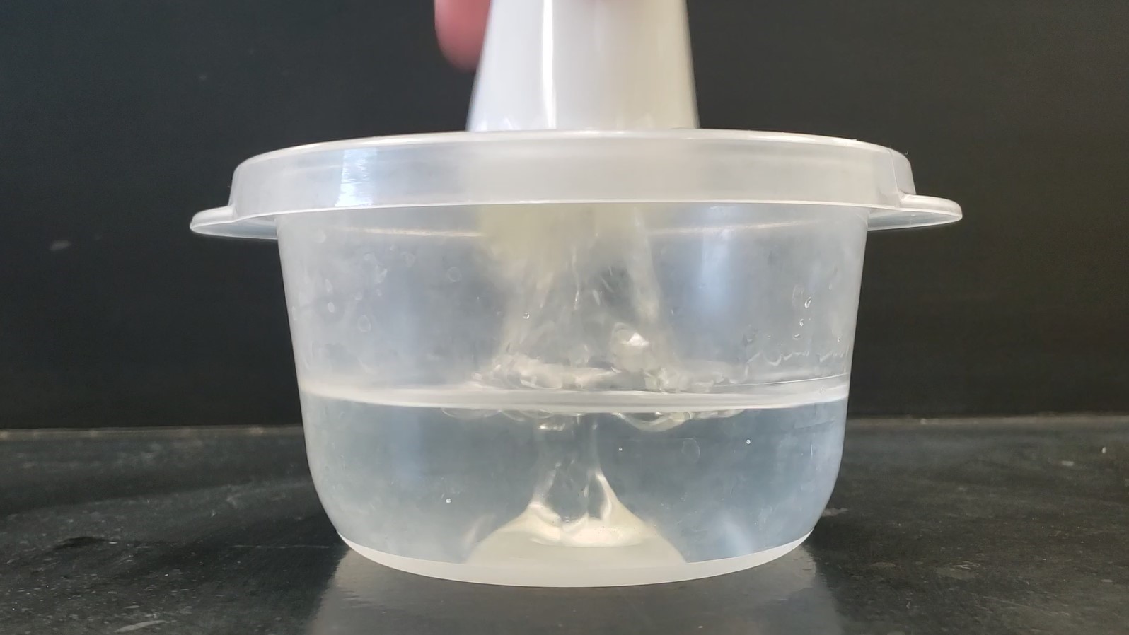 container filled with water and an upside down cup is being pulled out of the water resulting in oil entering the water 