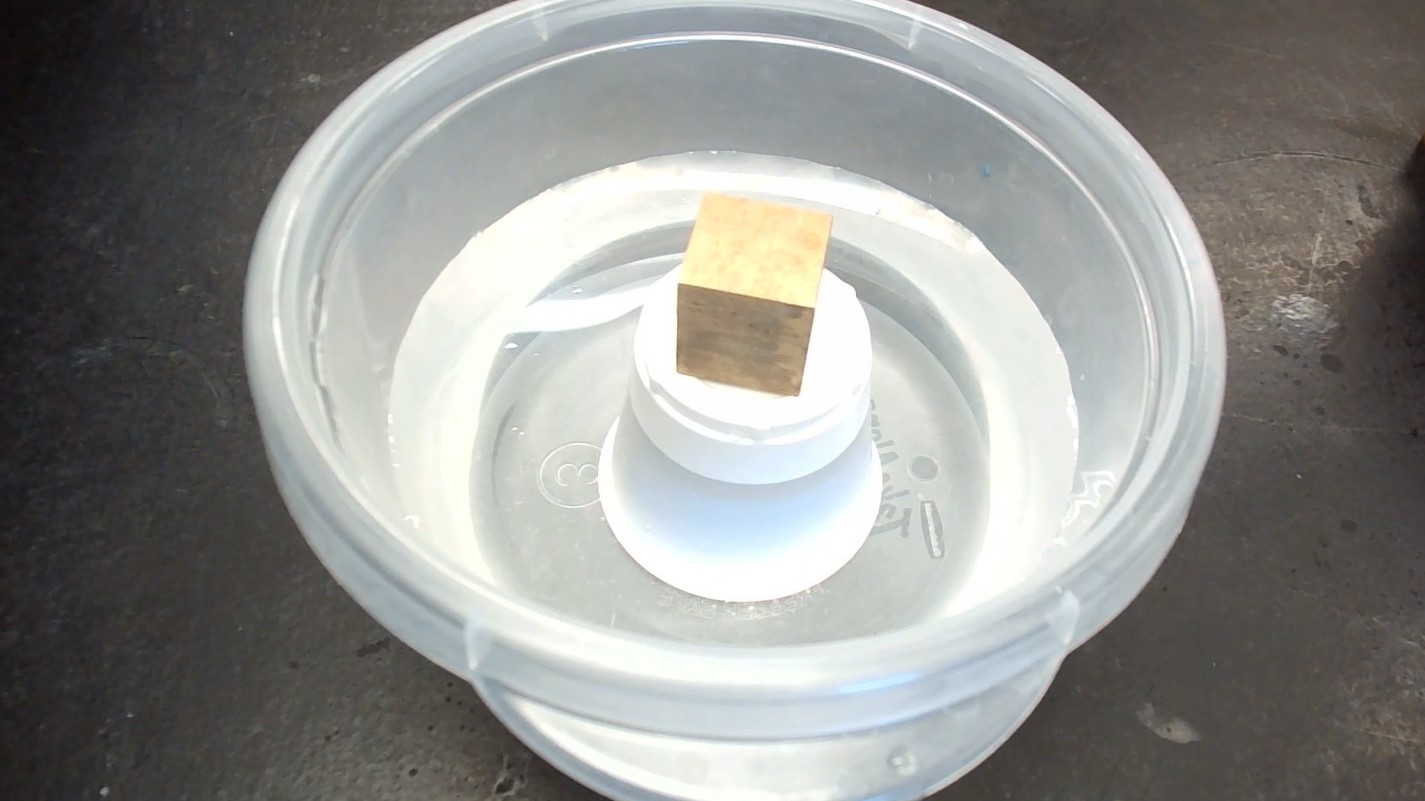 container filled with water and an upside down cup held down by a small gold colored weigh