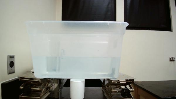 container of water propped up by four jacks and a cup of water underneath