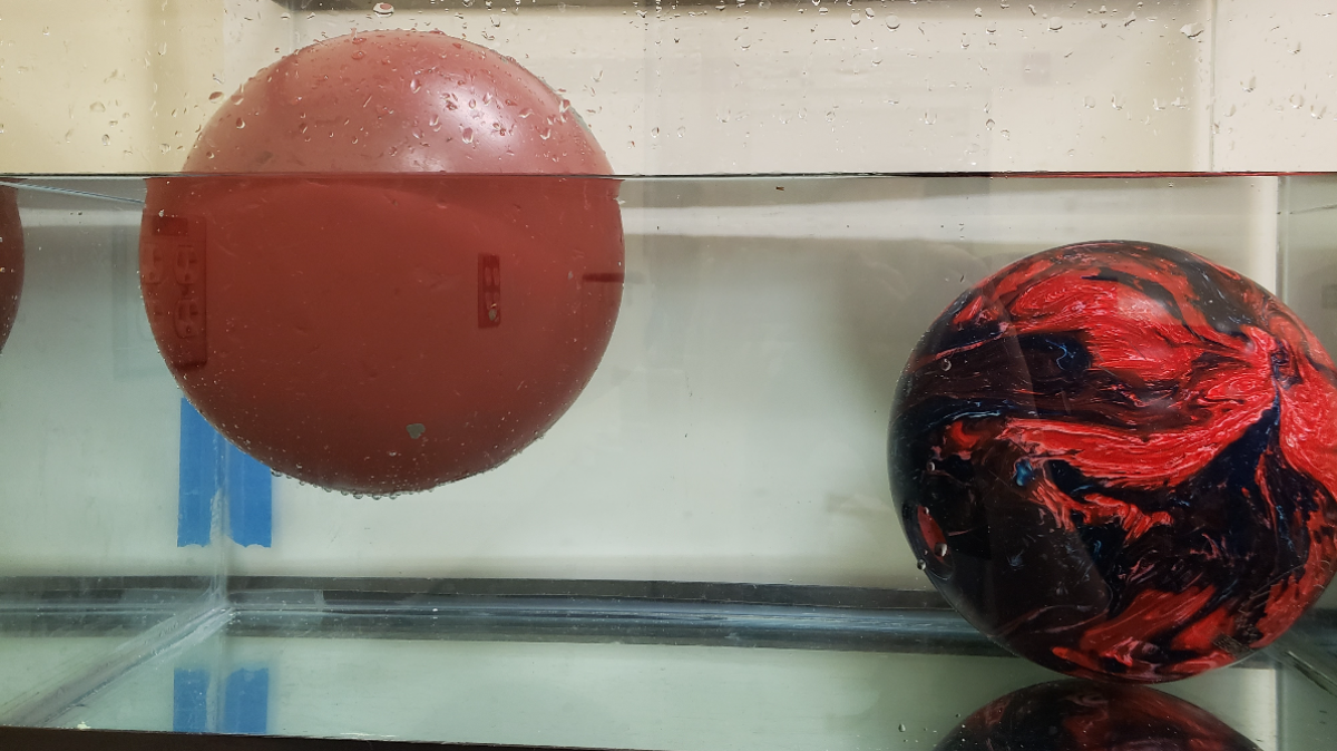 two bowling balls in a container of water, one is floating and the other is sinking