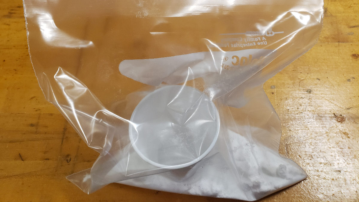 ziplock bag filled with baking soda and a small cup of vinegar