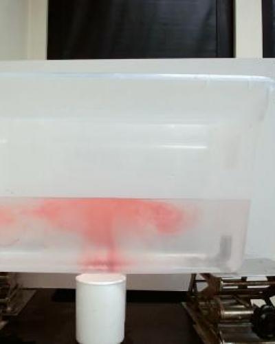 container of water with red food dye making a mushroom cloud shape with the container propped up by four jacks and a cup of water underneath